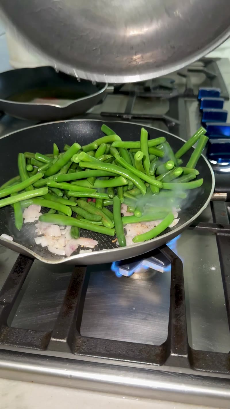 Green beans tossed with sautéed shallots in a skillet
