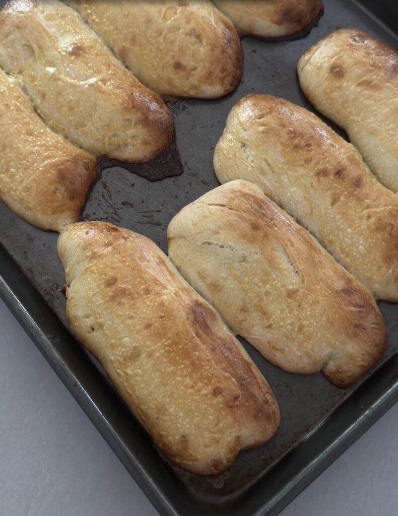 Tray of golden homemade sourdough sub rolls fresh from the oven