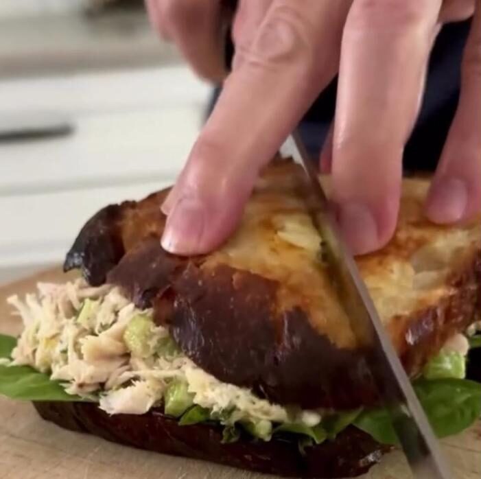 Cutting a tuna salad sandwich on toasted sourdough
