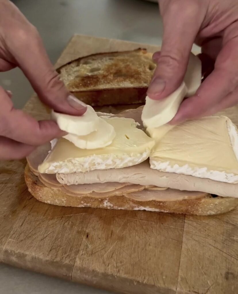 Layering sliced brie and fresh mozzarella over turkey on sourdough