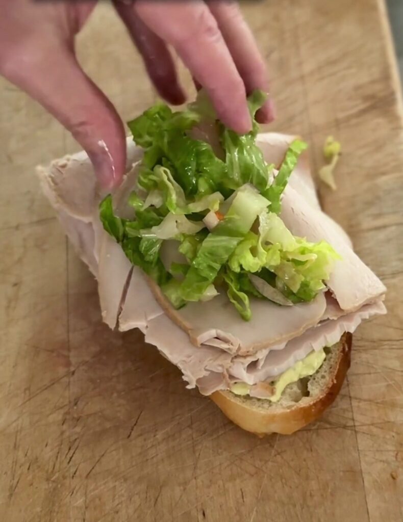 Piling dressed chopped salad on turkey for a sourdough sub